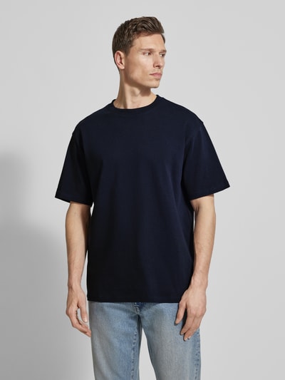 Männermodel trägt dunkelblaues Relaxed Fit T-Shirt aus Bio-Baumwoll-Mix Modell 'MAARKOS' von Armedangels, unifarben, Nahaufnahme Oberkörper.