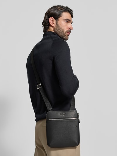 Männermodel trägt Umhängetasche mit Logo-Applikation in Leder-Optik von Emporio Armani, schwarze Farbe, Ganzkörperansicht Rückansicht. Hauptfach mit Reißverschluss, verstellbarer Schulterriemen 108 cm, 21x22x4 cm.