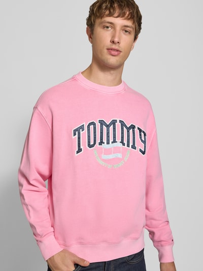 Männermodel trägt Relaxed Fit Sweatshirt aus reiner Baumwolle von Tommy Jeans in Rosa mit großem Logo, Ganzkörperansicht von vorne. Herren Sweatshirt von Tommy Jeans.