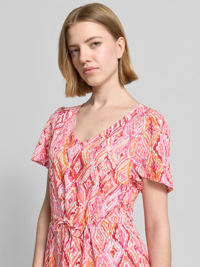 Frauenmodel trägt Tailliertes Freizeitkleid aus reiner Viskose Modell 'EASY JOY' von Vero Moda, Optik:Allover-Muster, V-Ausschnitt, Kurzarm, in leuchtenden Rosatönen mit grafischem Muster, Material: Viskose, Nahaufnahme Oberkörper.