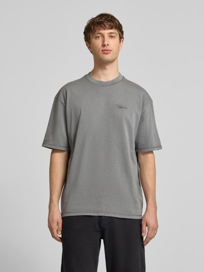 Männermodel trägt Oversized Fit T-Shirt mit Logo-Stitching von Pegador aus reiner Baumwolle in Grau, Rundhalsausschnitt, Ganzkörperansicht von vorne.