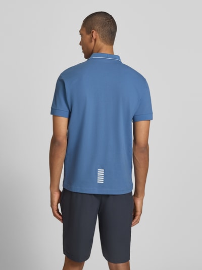 Mężczyzna nosi Regular Fit Poloshirt mit Logo-Print od EA7 Emporio Armani, niebieski bawełniany materiał, krótki rękaw, ujęcie całej sylwetki z tyłu.