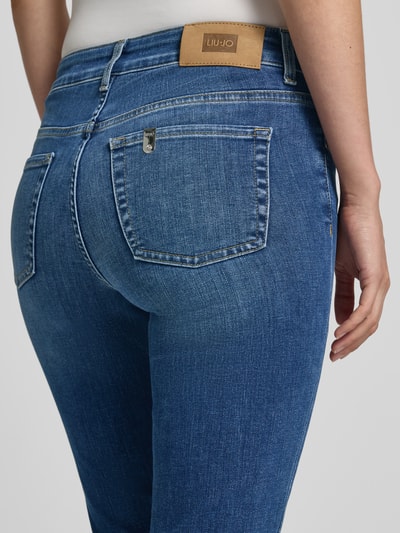 Frauenmodel trägt Flared Fit Jeans aus Baumwoll-Mix Modell 'Authentic' von Liu Jo White in mittlerem Blau, 5-Pocket-Design, Nahaufnahme Rückansicht. Damen Jeans von Liu Jo, elastischer Stoff, sichtbares Markenlabel, glatte Textur, Detailaufnahme.