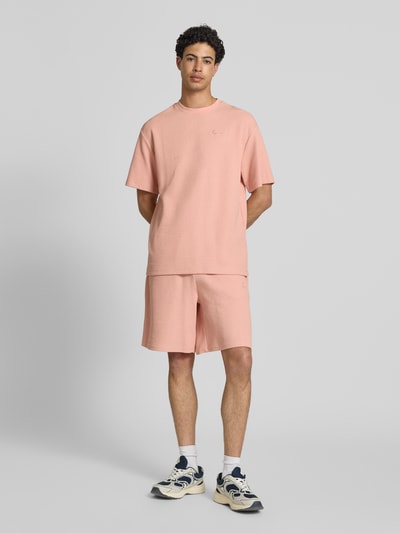 Männermodel trägt Oversized Fit T-Shirt mit Strukturmuster von KARL KANI in Rosé, Baumwoll-Mix, Logo-Stitching, Ganzkörperansicht von vorne.