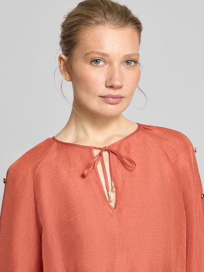 Frauenmodel trägt Bluse aus Leinen-Mix mit Zierknöpfen von Marc Cain in Orange, lockerer Schnitt, Schlüsselloch-Ausschnitt, Nahaufnahme Oberkörper.