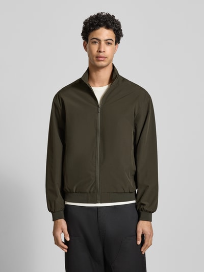 Männermodel trägt Regular Fit Jacke mit Stehkragen Modell 'Charge' von JACK & JONES in Oliv mit Reißverschluss, Eingrifftaschen, elastischen Abschlüssen, Ganzkörperansicht von vorne. Rückenlänge 66 cm, Schulterbreite 49 cm, Brustweite 50 cm, Ärmellänge 64 cm in Größe M.