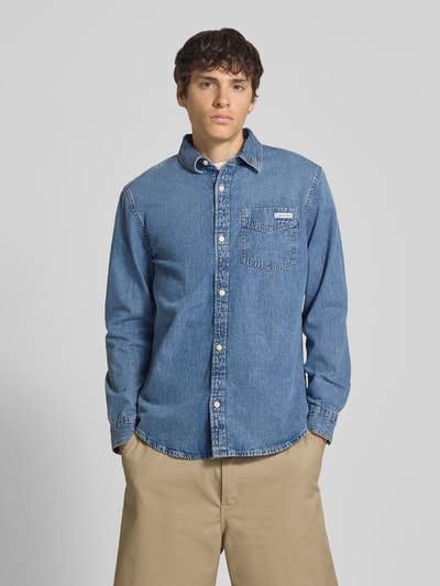 Männermodel trägt Regular Fit Jeanshemd aus reine Baumwolle von Calvin Klein Jeans in denimlook mit borstzak, lange mouw, kentkraag, doorlopende knoopsluiting, labelpatch; ganzkörperansicht von vorne.