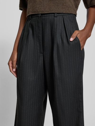 Frauenmodel trägt Stoffhose mit Bundfalten von black palms, dunkler Material-Mix mit Viskose-Anteil, französische Eingrifftaschen, Nahaufnahme Oberkörper.