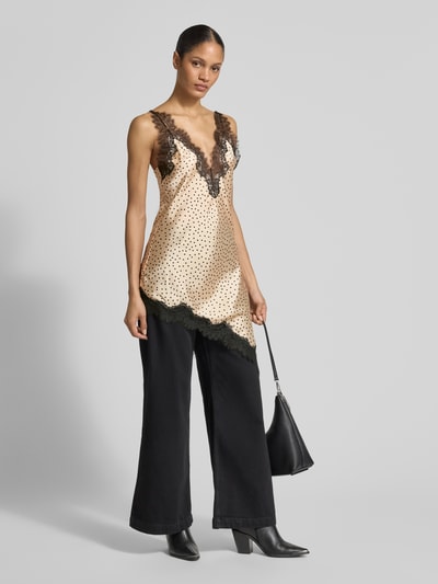 Frauenmodel trägt Top aus Satin in asymmetrischer Form Modell 'SILVER' von Mango mit Spitzenbesatz, V-Ausschnitt, Regular-Fit, Rückenlänge bei Größe S 52 cm, beige mit schwarzen Punkten, Glanzstruktur, weiche Haptik, Ganzkörperansicht von vorne.