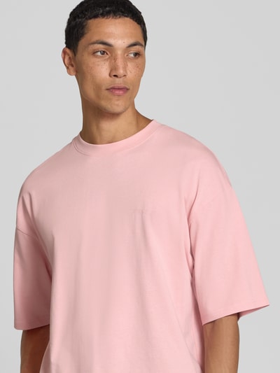 Męski model nosi Oversized T-Shirt aus reiner Baumwolle od REVIEW, kolor jasnoróżowy, okrągły dekolt, nadruk z logo, bawełna, krój oversized, długość tyłu w rozmiarze M: 66 cm, ujęcie z przodu, zbliżenie na górną część ciała.
