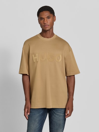 Mannelijk model draagt Regular Fit T-shirt uit zuivere katoen model 'Dinkee' van HUGO in beige met grote logo-opdruk, Heren t-shirt van HUGO, volledig lichaam vooraanzicht.
