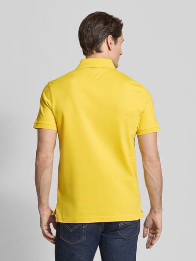 Männermodel trägt Regular Fit Poloshirt aus Baumwoll-Mix von Tommy Hilfiger in Uni-Gelb, Piqué-Textur, Rückansicht Ganzkörperansicht.