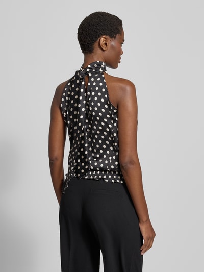 Frauenmodel trägt Blusentop im Allover-Look von Neo Noir in Schwarz mit weißen Punkten, Stehkragen und rückseitiger Schnürung, Ganzkörperansicht Rückansicht.