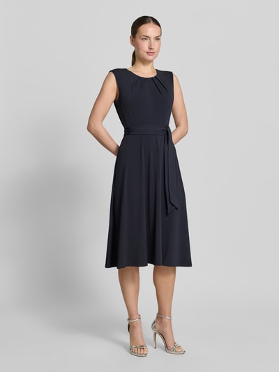 Modelka nosi Cocktailkleid mit Bindegürtel von Christian Berg Woman Selection, granatowa, elastyczna, taliowany krój, długość midi, okrągły dekolt, drapowania, pasek, długość tyłu w rozmiarze 36: 105 cm, szerokość w rozmiarze 36: 33 cm, widok całej sylwetki z przodu