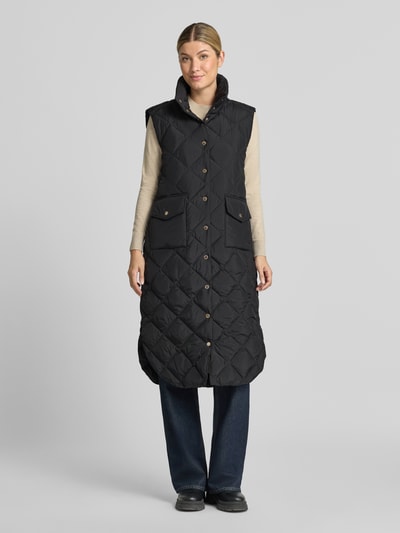 Vrouwenmodel draagt zwarte bodywarmer in stiksels, regular fit, opstaande kraag, opgestikte zakken, FREE/QUENT Model 'Olga', Ganzkörperansicht von vorne. Ruglengte maat S: 113 cm, schouderbreedte: 44 cm, borstwijdte: 54 cm.