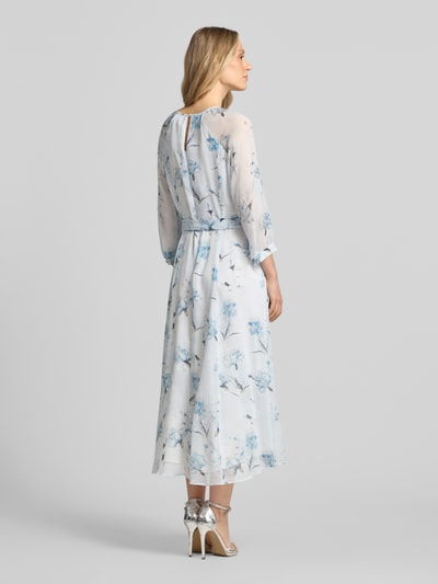 Frauenmodel trägt Midikleid mit Bindegürtel von More & More in Weiß mit blauen Blumen, transparenter 3/4-Arm, Ganzkörperansicht Rückansicht, taillierter Schnitt, Rundhalsausschnitt mit Cut-Out, rückseitiger Schlüsselloch-Ausschnitt, Reißverschluss, Rückenlänge 128 cm, Brustweite 42 cm, Ärmellänge 58 cm.