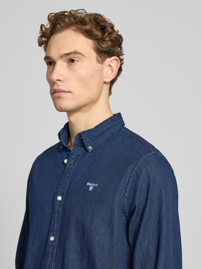 Männermodel trägt Slim Fit Jeanshemd aus reiner Baumwolle von Barbour, tkanina stylizowana na denim, długi rękaw, wyhaftowane logo, kołnierzyk typu button down, listwa guzikowa na całej długości, mankiet zapinany na 1 guzik, materiał: bawełna, kolor ciemnoniebieski, Nahaufnahme Oberkörper.