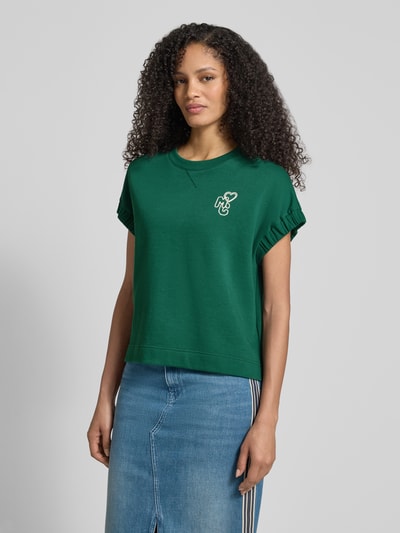 Frauenmodel trägt Relaxed Fit T-Shirt mit Logo-Detail von Marc Cain in Grün, Baumwoll-Mix, Rundhalsausschnitt, Oberkörperansicht von vorne.