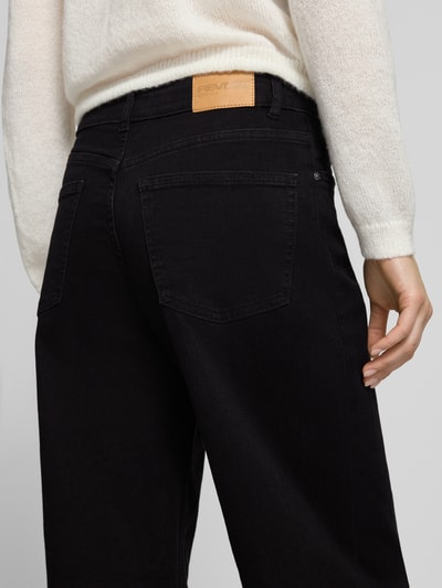 Kobiece modelka nosi Wide-Leg-Jeans mit mittelhohem Bund od Review, czarny bawełniany miks z dodatkiem stretchu, luźny krój, 5 kieszeni, zamek i guzik, szerokość w rozmiarze 27: 39 cm, długość wewnętrzna nogawki: 80 cm, detal z tyłu zbliżenie.