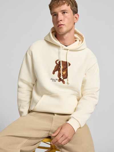 Mężczyzna nosi Relaxed Fit Hoodie aus Baumwoll-Mix mit Hunde-Patch od REVIEW, mieszanka bawełny, krój relaxed fit, naszywka z psem, wyhaftowane logo, krój z długim rękawem, prążkowane wykończenia, kaptur z tunelem, beżowy kolor, długość tyłu w rozmiarze M: 68 cm, długość rękawów w rozmiarze M: 71 cm, pełen widok z przodu.
