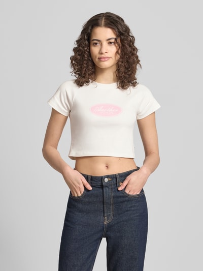 Frauenmodel trägt Cropped T-Shirt mit Logo-Print von ANOTHER COTTON LAB in Weiß, reine Baumwolle, Rundhalsausschnitt, Ganzkörperansicht von vorne.