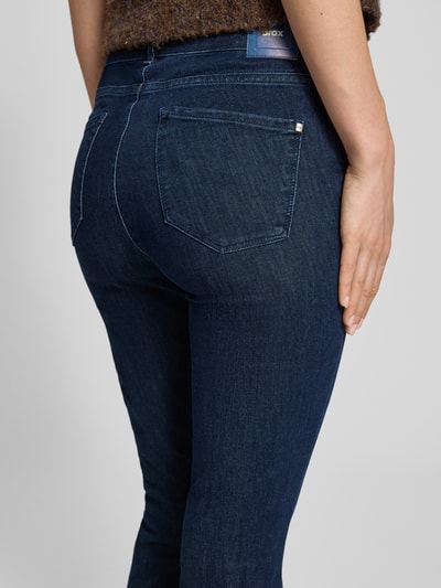 Frauenmodel trägt Bootcut Jeans mit Fransen Modell 'SHAKIRA' von Brax aus dunkelblauem Baumwoll-Mix mit Stretch-Anteil, Gesäßtaschen, Verkürzte Passform, Nahaufnahme Rückansicht.