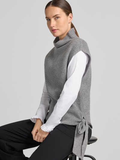 Frauenmodel trägt Relaxed Fit Pullunder aus reinem Kaschmir mit Stehkragen von Christian Berg Woman in Grau mit Zierschleife, Nahaufnahme Oberkörper.