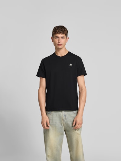 Mannenmodel draagt Regular Fit T-shirt met logodetail van Moose Knuckles, puur katoen, ronde hals, korte mouw, ruglengte maat M 67 cm, geheel zwarte kleur, gladde textuur, regular fit, geheel vooraanzicht.