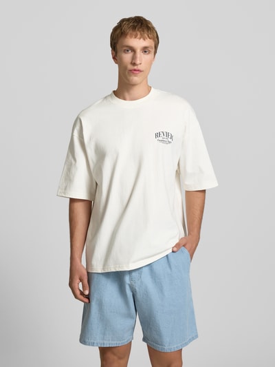 Männermodel trägt T-Shirt mit Label-Detail von REVIEW in Weiß aus reiner Baumwolle, lockerer Schnitt, Rundhalsausschnitt, Halbarm, Nahaufnahme Oberkörper.