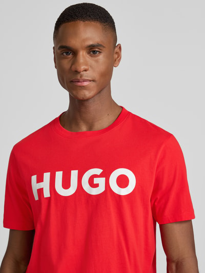 Männermodel trägt T-Shirt mit Label-Schriftzug Modell 'DULIVIO' von HUGO, rood, katoen, rechte pasvorm, close-up bovenlichaam.