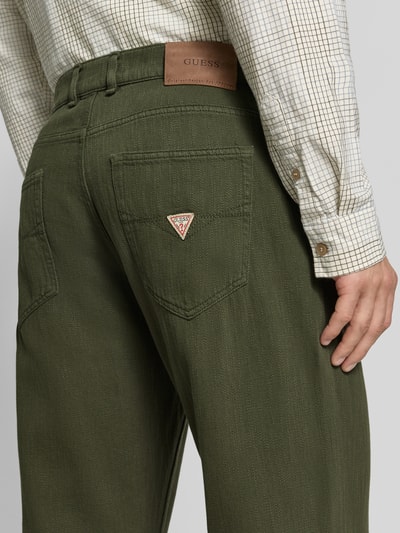 Männermodel trägt Relaxed Fit Jeans mit Eingrifftaschen Modell 'DAMON' von GUESS in Olivgrün, Struktur sichtbar, Nahaufnahme Rückansicht. Baumwolle, Gesäßtaschen, Bundweite 44 cm, Innenbeinlänge 78 cm.