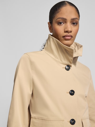 Kobiece modelka nosi Jacke mit Stehkragen und Pattentaschen von Christian Berg Woman Selection, beżowy kolor, krój regular fit, stebnowane guziki, patki na kieszeniach, długość tyłu 60 cm w rozmiarze 36, szerokość ramion 40 cm w rozmiarze 36, szerokość klatki piersiowej 46 cm w rozmiarze 36, długość rękawa 67 cm w rozmiarze 36, zbliżenie na górną część sylwetki.