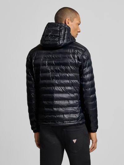 Męski model nosi Kurtka pikowana z zamkiem błyskawicznym dwustronnym Model 'Charles' od Blauer Usa, krój regular fit, kaptur, detal z logo, długość tyłu w rozmiarze M: 65 cm, szerokość ramion w rozmiarze M: 47 cm, szerokość w rozmiarze M: 55 cm, długość rękawów w rozmiarze M: 65 cm, ciemnogranatowa, błyszcząca faktura, poziome przeszycia, widok całej sylwetki z tyłu.
