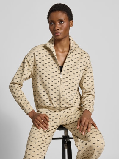 Frauenmodel trägt Sweatjacke mit Reißverschluss von Armani Exchange aus Baumwoll-Mix, beiger Stoff mit Allover-Label-Print, Nahaufnahme Oberkörper.