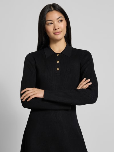 Modelka kobieca ma na sobie czarną sukienkę z dzianiny 'Tailliertes Strickkleid aus Viskose-Mix' od Jake*s Collection, tekstura prążkowana, zapięcie na guziki, zbliżenie górnej części ciała.