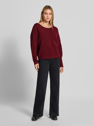 Frauenmodel trägt Relaxed Fit Strickpullover aus Material-Mix mit Leinen-Anteil von American Vintage in Dunkelrot, Struktur grob, kombiniert mit schwarzer weiter Hose, Pullover mit gerippten Abschlüssen und überschnittenen Schultern, Damen Strickpullover, Langarm, Rundhalsausschnitt, Ganzkörperansicht von vorne.