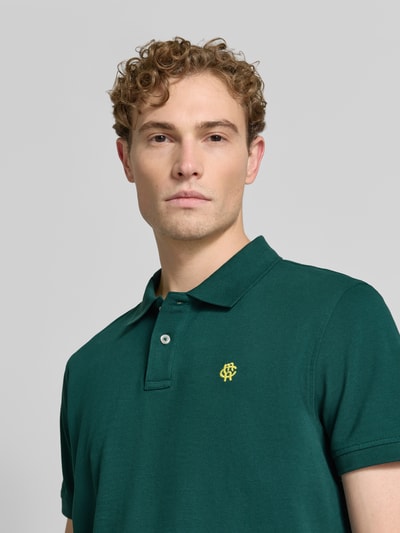Męski model nosi Regular Fit Poloshirt mit Label-Stitching von MCNEAL z bawełny, krój regular fit, listwa guzikowa, długość tyłu 70 cm w rozmiarze M, kolor zielony, wyraźna tekstura materiału, wyhaftowane logo, zbliżenie na górną część tułowia, widok z przodu.