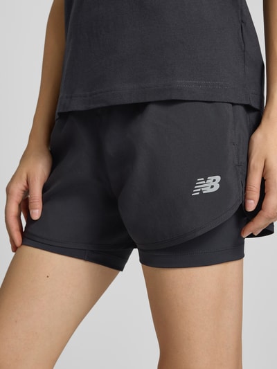 Frauenmodel trägt schwarze Shorts im 2-in-1-Look mit Logo von New Balance, elastischer Bund, Nahaufnahme Oberschenkel, Regular Fit.