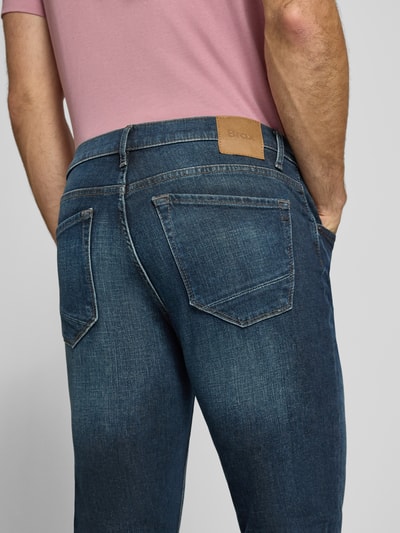 Männermodel trägt Modern Fit Jeans aus Baumwoll-Mix Modell 'Chuck' von Brax, Denim-Optik mit Label Patch, Ganzkörperansicht Rückansicht.