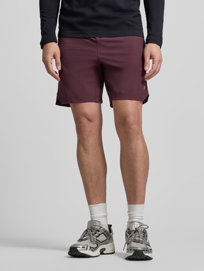 Männermodel trägt Regular Fit Shorts mit Logo-Print von Fabletics in Dunkelrot, elastischer Bund, sportlicher Look, Nahaufnahme Beine, Vorderansicht.