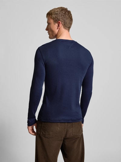 Męski model nosi Slim Fit Longsleeve mit Rippenstruktur od Tommy Jeans, bawełna, okrągły dekolt, krój slim fit, wyhaftowane logo, długość tyłu 73 cm, długość rękawów 68 cm, prążkowana faktura, widok całej sylwetki od tyłu.