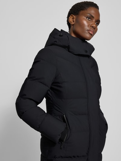 Vrouwenmodel draagt Daunenmantel mit Kapuze van Moose Knuckles in zwart, getailleerd, met stretch, kap en ritszakken, close-up bovenlichaam.