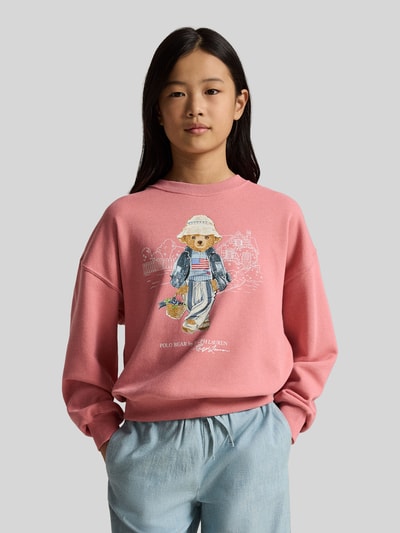 Dziewczynka nosi Regular Fit Sweatshirt aus Baumwoll-Mix mit BEAR-Motiv od Polo Ralph Lauren Teens, efekt: jednolity kolor, krój regular fit, aplikacja: polo bear, z napisem z logo, okrągły dekolt, długi rękaw z prążkowanym wykończeniem, wykończenie z dzianiny dresowej, mieszanka bawełny, bluza, przód w całości, tło szare. Ganzkörperansicht von vorne.