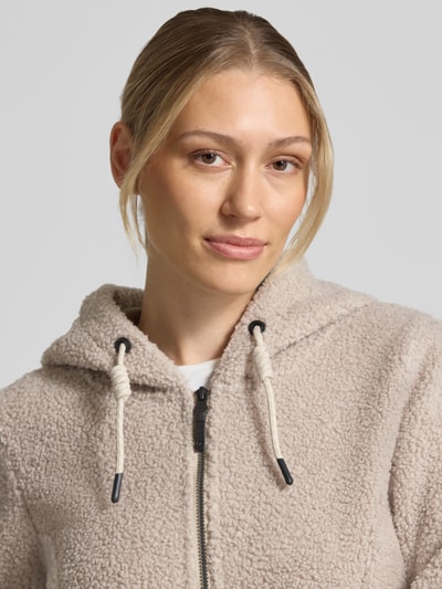 Vrouwenmodel draagt Mantel aus Strickfleece van G.I.G.A. DX in beige met capuchon en tunnelkoord, steekzakken, tweewegritssluiting, getailleerde pasvorm, tricotfleece structuur, Ruglengte maat 36: 67 cm, Schouderbreedte: 43 cm, Borstwijdte: 48 cm, Mouwlengte: 62 cm, Nahaufnahme bovenlichaam.