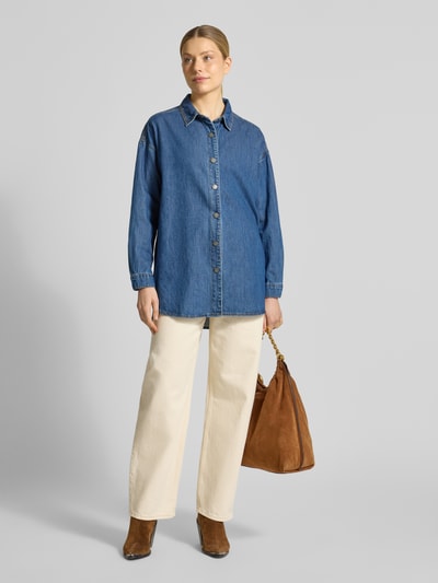 Frauenmodel trägt Oversized Jeansbluse mit überschnittenen Schultern Modell 'Hilma' von My Essential Wardrobe, reine Baumwolle, Umlegekragen, blaue Farbe auf weißer Hose, Ganzkörperansicht von vorne.