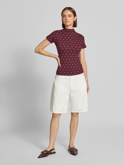 Vrouwenmodel draagt Slim Fit T-Shirt uit katoenmix van Marc O'Polo DENIM, bordeaux met witte stippen, witte bermuda, volledige frontale lichaamsopname.