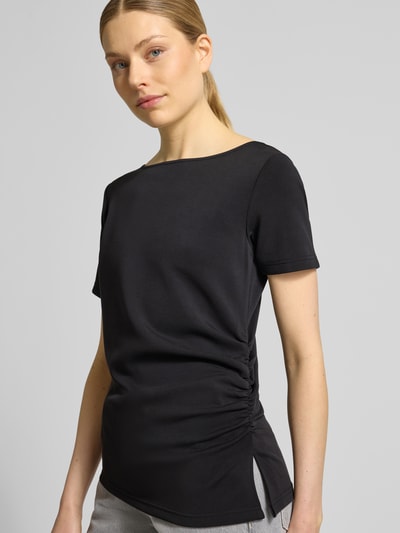 Modelka nosi damski t-shirt w asymetrycznym kroju, model 'Helle' od My Essential Wardrobe, mieszanka materiałów z dodatkiem wiskozy, okrągły dekolt, drapowania, długość tyłu w rozmiarze S: 60 cm, widok całej sylwetki z przodu.