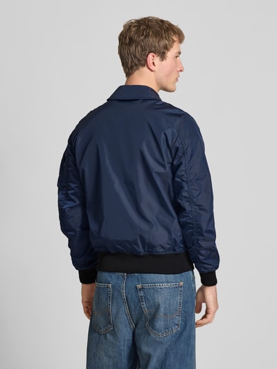 Männermodel trägt Regular Fit Bomberjacke mit Logo-Patch von Alpha Industries in Dunkelblau, elastische Abschlüsse, Umlegekragen, Ganzkörperansicht Rückansicht