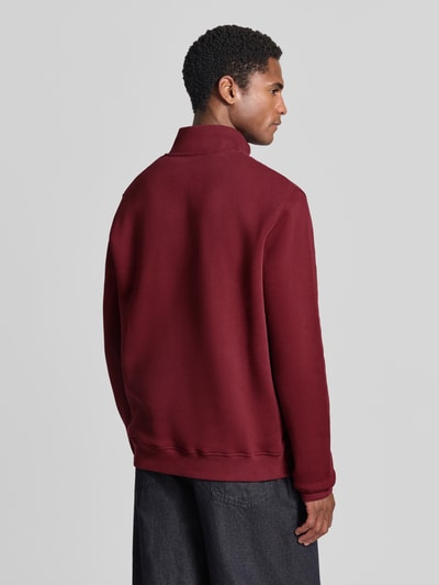 Männermodel trägt Regular Fit Troyer aus reiner Baumwolle Modell 'WAARLO' von ARMEDANGELS in Dunkelrot, glatte Textur, Ganzkörperansicht Rückansicht.