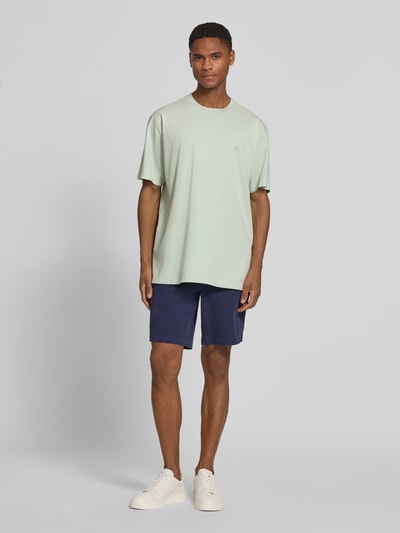 Männermodel trägt Relaxed Fit T-Shirt aus reiner Bio-Baumwolle Modell 'ICONIC MAARKOS GD' von Armedangels in Hellgrün, unifarben, Jersey-Struktur, Logo-Print, mit Rundhalsausschnitt und kurzen Ärmeln, Ganzkörperansicht von vorne.